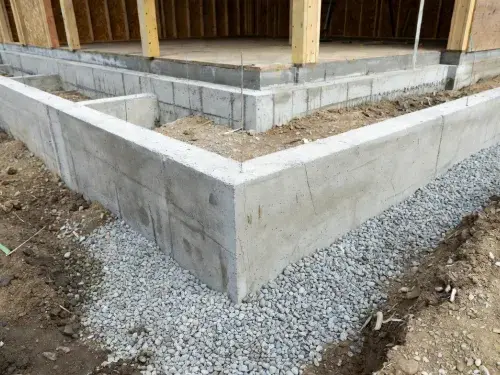 Poured concrete house foundation corner with gravel base at a residential jobsite.