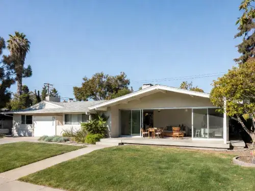 Modern addition to a ranch house with a new gabled living volume and wide sliding glass opening.