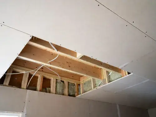 Opened ceiling showing joists, insulation, wiring, and drywall in a residential room.