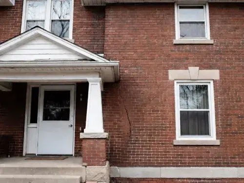 Brick house exterior with a diagonal settlement crack running toward the foundation.