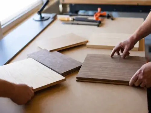 Wood boards laid out for comparison on a workshop table while hands evaluate grain, color, and type.
