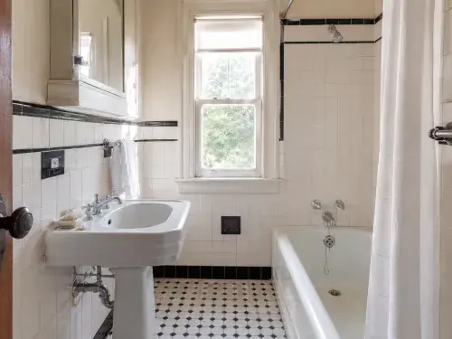 Preserved 1930s bathroom with black-and-white tile, pedestal sink, tub, and chrome fixtures.