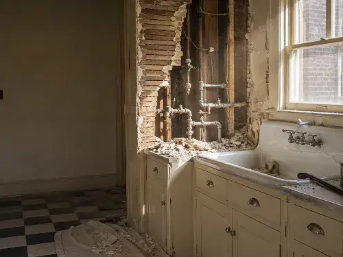 1930s kitchen demolition day with open lath-and-plaster wall, exposed plumbing, enamel sink, and checkerboard floor.