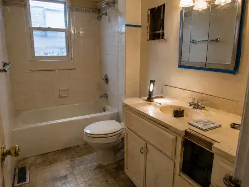 1960s bathroom before remodel with old wall tile, tub-shower, worn flooring, dated vanity, open access area, flashlight, tape measure, and sample tile.