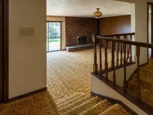 1970s split-level house interior with shag carpet, railing, brick fireplace, and wood paneling.