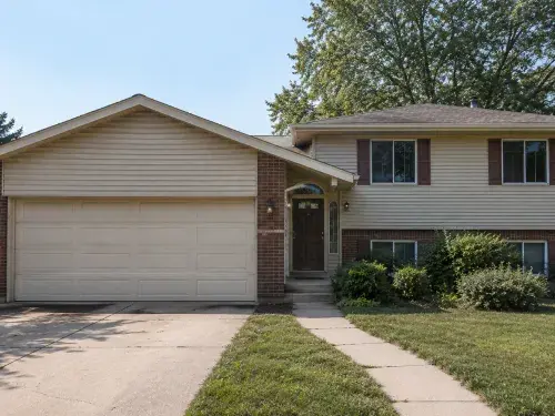 1980s split-level house exterior with dominant garage, beige siding, brick, and modest entry.