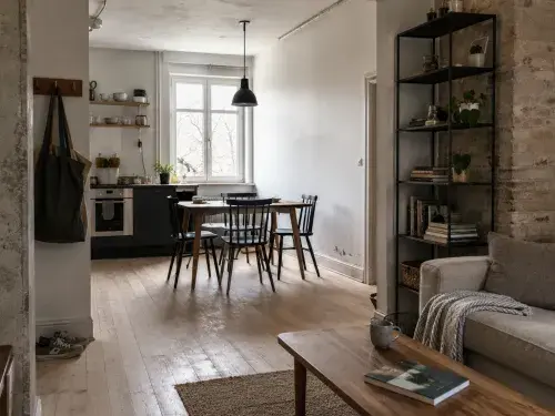 Scandinavian industrial apartment with brick, black metal shelving, pale wood, sofa, shoes, and daylight.