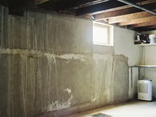Older basement wall with damp staining, floor drain, and dehumidifier.