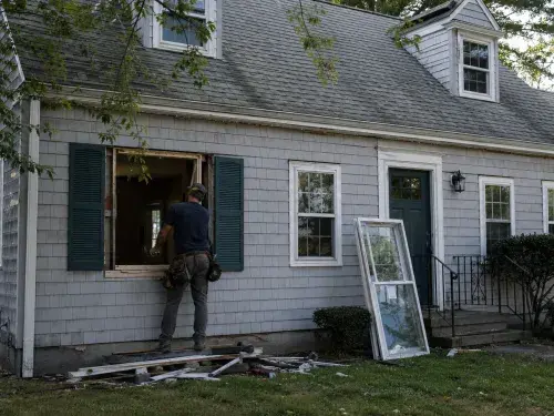Cape Cod house during window replacement with an open window bay and worker outside.