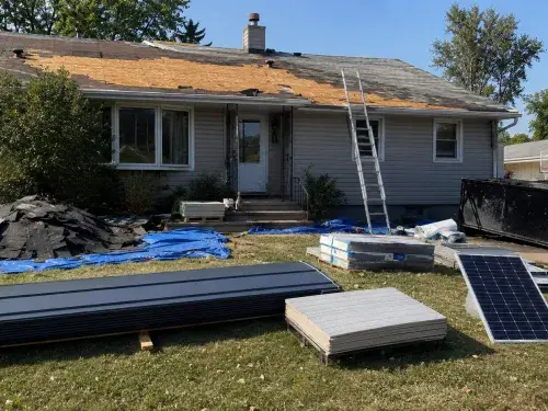 House roof replacement with exposed sheathing, staged metal roofing, reflective roofing, and solar panel planning materials.