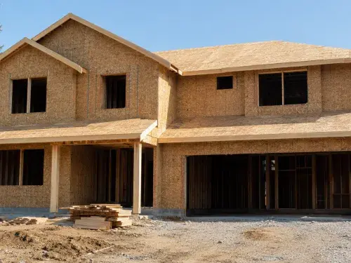 Two-story house under construction with OSB wall and roof sheathing visible.