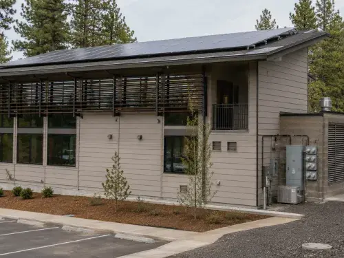 Low-energy building with rooftop solar panels, exterior shading, high-performance windows, and visible mechanical service equipment for net zero architecture.