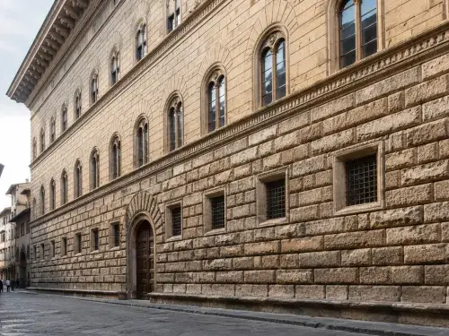 Renaissance urban palace facade on a narrow Italian street with rusticated stone base, ordered upper windows, deep shadows, and small pedestrians for scale.