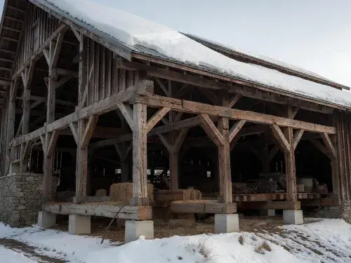 Wooden barn frame carrying roof snow load with posts, beams, braces, and foundation supports.