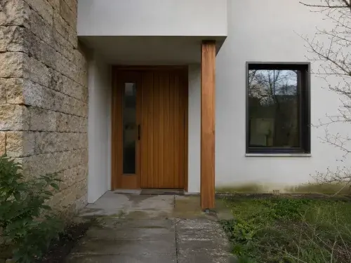 House entry with rough stone, smooth stucco, wood door, glass, and worn paving.