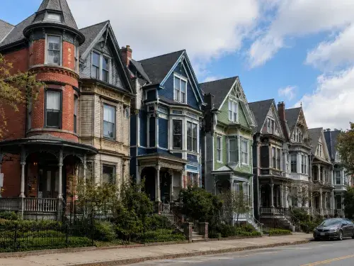 Street of Victorian houses with steep rooflines, bay windows, porches, tall windows, and decorative trim.