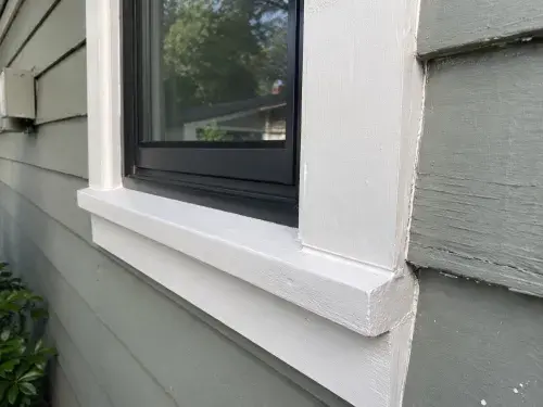 Close-up of replacement window casing, sill, and siding detail in daylight.