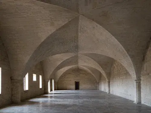 Stone hall with repeated groin vaults spanning an open floor between heavy masonry supports.