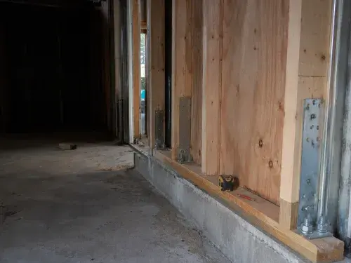 Seismic retrofit framing with plywood shear panels, hold-down anchors, and concrete foundation.