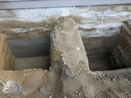 Completed and open underpinning bays separated by untouched soil beneath a foundation.