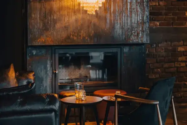 Rustic living room with a fireplace, wall behind it featuring chandeliers and armchairs nearby.