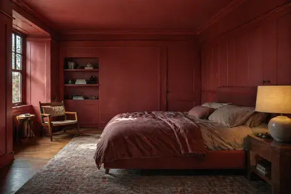 A fully red bedroom where every element matches, featuring a regretful couple sitting on the bed, realizing their design mistake.