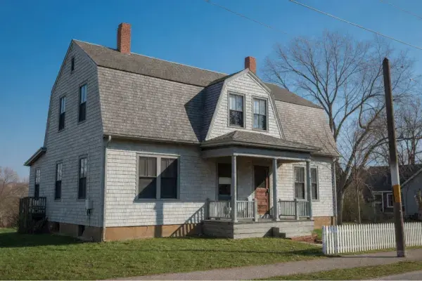 Showing Dutch Colonial Revival home with shingle siding, gambrel roof, and white picket fence in color.
