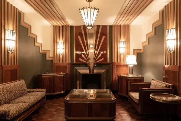 Art Deco sitting room with stepped wall geometry, polished wood paneling, symmetrical lighting, and a sunburst fireplace design.