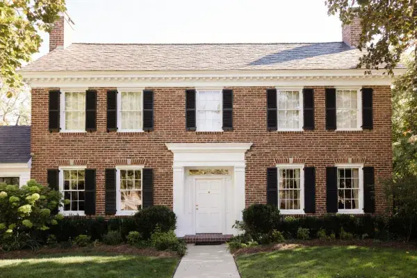 Classic brick colonial house with centered doorway, black shutters, and symmetrical windows.