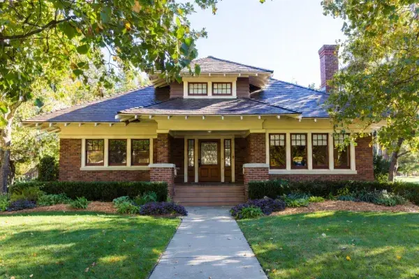 Front view of a Craftsman bungalow with a broad porch, exposed rafters, and brick piers.