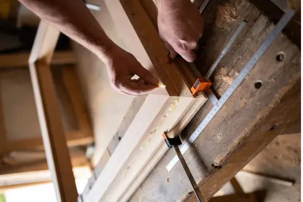 Hands assembling a DIY wood window frame on a country workshop bench.