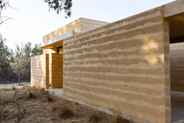 Finished rammed earth building with thick layered walls in a dry site setting.
