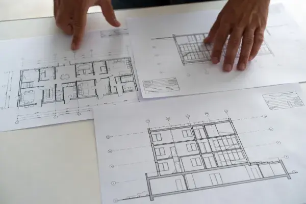 Person reviewing printed blueprint drawings on a table.