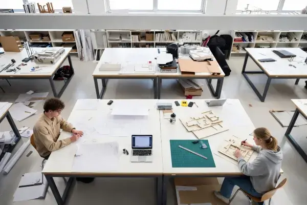 Architecture students working in a design studio with drawings, models, and critique boards.