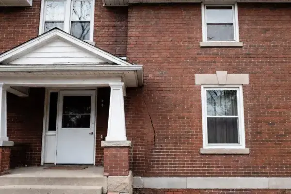 Brick house exterior with a diagonal settlement crack running toward the foundation.