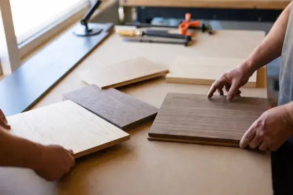 Wood boards laid out for comparison on a workshop table while hands evaluate grain, color, and type.