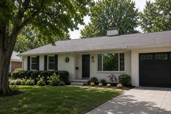 Updated ranch house exterior with white brick, black shutters, a dark garage door, low roofline, and restrained front landscaping.