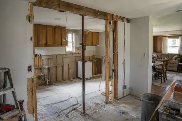 Ranch kitchen wall removal with temporary support, exposed studs, beam area, wiring, protected floor, and living room beyond.
