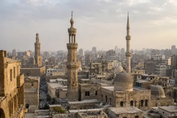Historic Islamic city skyline with mosque minarets rising above domes, courtyards, rooftops, and narrow streets.
