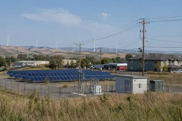 Solar panels, wind turbines, utility lines, service equipment, and nearby buildings showing how renewable energy connects to real infrastructure.