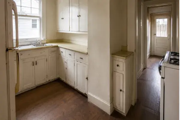 Unrenovated 1920s bungalow kitchen with worn cabinets, laminate counters, and a narrow layout.