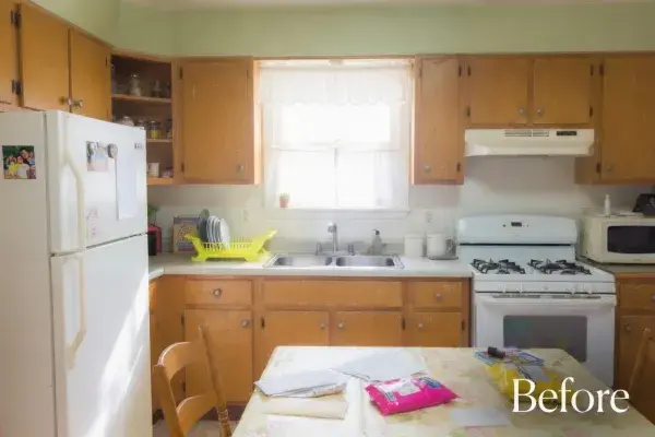 Worn midcentury kitchen with wood cabinets, white appliances, and a crowded dining table.