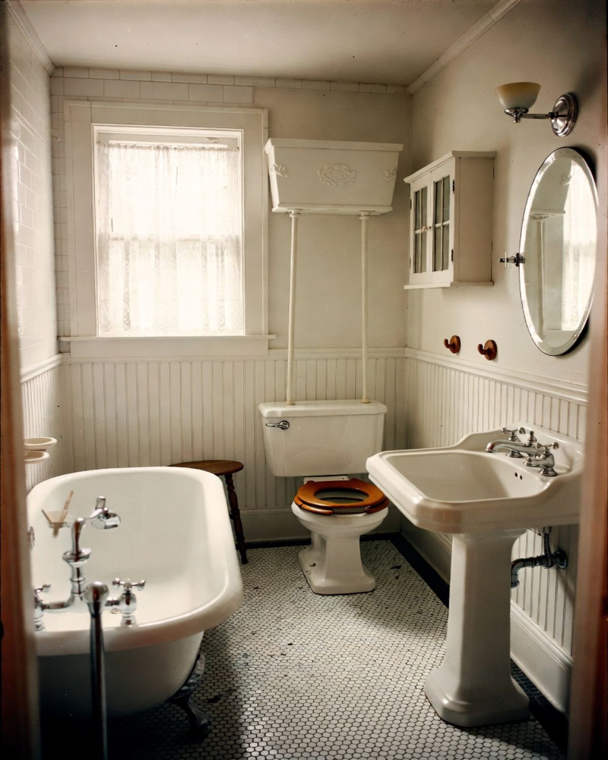 1910s bathroom with clawfoot tub, pedestal sink, high-tank toilet, beadboard walls, and hex tile floor.